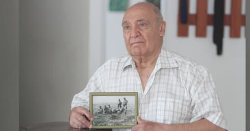 עזרא משקיף-עינצ'י מחזיק את תמונת אחיו וחבריו לנשק | צילום: אסף פרידמן