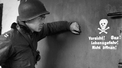 En esta foto de archivo tomada el 29 de abril de 1945, un soldado estadounidense mira un cartel frente a la puerta de una cámara de gas en el campo de concentración de Dachau (AFP) Fotos Shoá