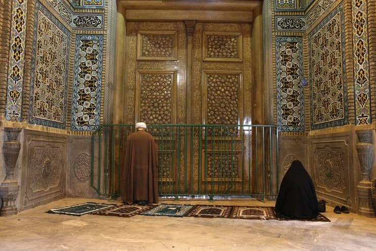 Un clérigo y una mujer rezan afuera del santuario de Masoume en Qom 