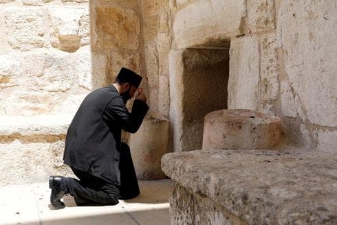 Un sacerdote se arrodilla afuera de la Iglesia de la Natividad cerrada debido a COVID-19 