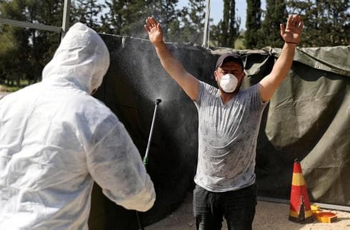 Trabajador sanitario palestino rocía desinfectante a un trabajador que regresa de Israel. 