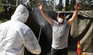 Trabajador sanitario palestino rocía desinfectante a un trabajador que regresa de Israel. 