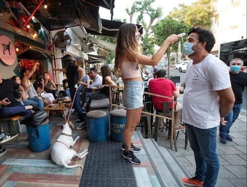 Una trabajadora verifica la temperatura de un cliente al ingresar a un bar en Tel Aviv. 