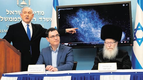 El primer ministro Benjamín Netanyahu, el exdirector general del Ministerio de Salud, Moshe Bar-Siman-Tov, y el exministro de Salud, Yaakov Litzman, hablando en el pico del brote. (Ynet ) El primer ministro Benjamín Netanyahu, el director general del Ministerio de Salud, Moshe Bar-Siman-Tov, y el ministro de Salud, Yaakov Litzman, hablando en el pico del brote.