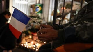 Un hombre sostiene una bandera de Francia y un rosario frente a la basílica de Notre-Dame.