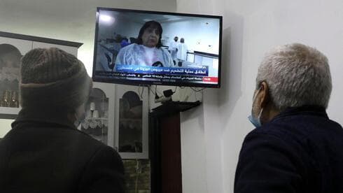Palestinos miran en Hebrón la transmisión de televisión en vivo de la ministra de Salud, Mai al-Kaila, anunciando el lanzamiento de la campaña de vacunación contra el COVID-19. (AFP) Los palestinos miran la transmisión de televisión en vivo de la ministra de Salud palestina, Mai al-Kaila, anunciando el lanzamiento de la campaña de vacunación contra el COVID-19 en la ciudad de Hebrón, en Cisjordania.