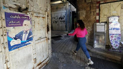 Una mujer camina junto a un antiguo cartel de campaña de Ali Salam en la Ciudad Vieja de Nazaret. 