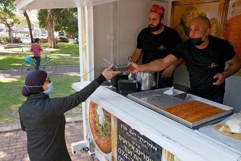 Una mujer recibe una rebanada de knafeh después de vacunarse contra el coronavirus en Tel Aviv. (AFP) Una mujer recibe una rebanada de knafeh después de vacunarse contra el coronavirus en Tel Aviv.