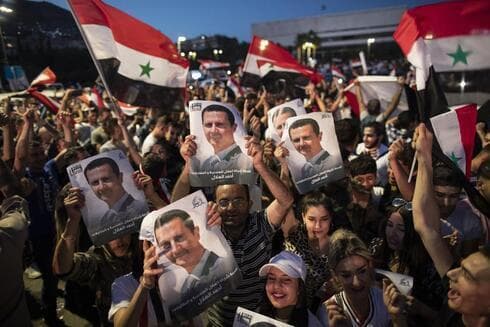 Partidarios del presidente sirio Bashar Assad sostienen banderas nacionales y fotos de Assad mientras celebran en la Plaza Omayyad, en Damasco. (AP) Partidarios del presidente sirio Bashar Assad sostienen banderas nacionales y fotos de Assad mientras celebran en la Plaza Omayyad, en Damasco.