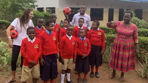 Ayelet posa con una pelota de fútbol con niños huérfanos de Tanzania vestidos con uniforme escolar. (Gentileza) Ayelet con huérfanos en Tanzania.