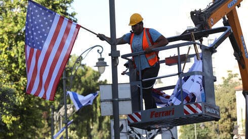 Un trabajador municipal de Jerusalem cuelga una bandera de EE.UU. antes de la llegada de Biden. 