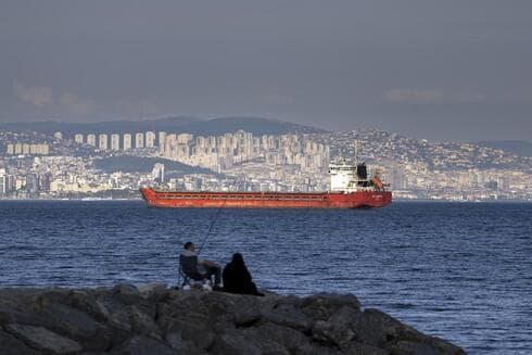 Una familia sentada en una roca frente a un buque de carga anclado en el Mar de Mármara espera el acceso para cruzar el Estrecho del Bósforo en Estambul, Turquía, el 13 de julio de 2022. (AP) Una familia sentada en una roca frente a un buque de carga anclado en el Mar de Mármara espera el acceso para cruzar el Estrecho del Bósforo en Estambul, Turquía, el 13 de julio de 2022.