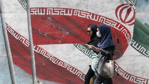 Mujeres iraníes pasan junto a una pintura mural de la bandera nacional de Irán en una calle del centro de Teherán.