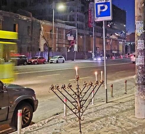 Una menorá encendida frente a los edificios dañados por los bombardeos rusos en Kiev. (Ynet) Una menorá encendida frente a los edificios dañados por los bombardeos rusos en Kiev.