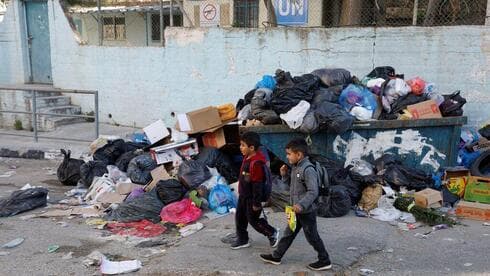 Niños palestinos pasan junto a un montón de basura en el campo de refugiados de Al Jalazone, cerca de Ramala, en Cisjordania, el 25 de enero de 2023. 