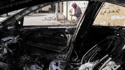 Una mujer camina junto a un vehículo incendiado en Jenín.