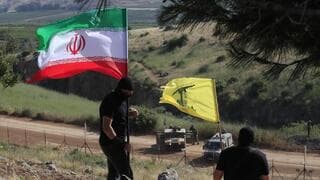 Dos hombres ondean las banderas de Irán y Hezbolá junto a la frontera israelí.