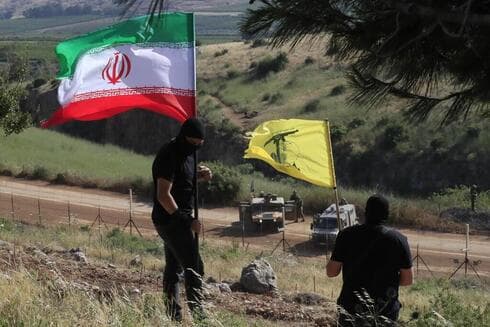 Dos hombres ondean las banderas de Irán y Hezbolá junto a la frontera israelí.