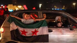 Una familia siria festeja desde su auto con una bandera del país. 